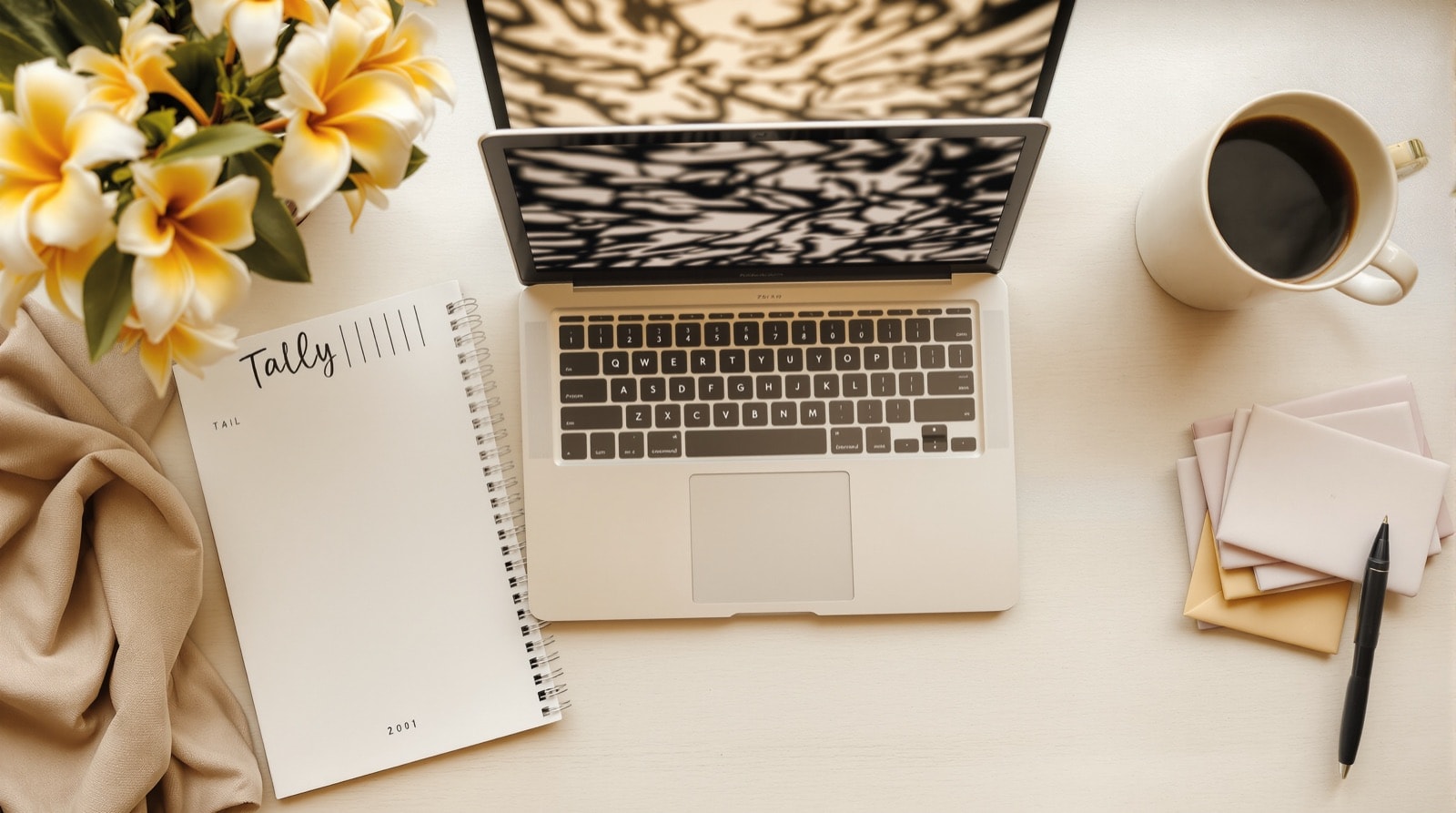 A desk with a laptop, a notebook of tally marks and a stack of gift envelopes